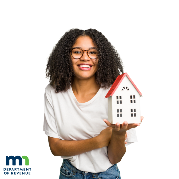 Young woman with glasses smiling and holding a model of a two-story home.